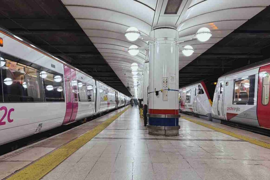 Platform of a metro station with trains on both sides, a central white pillar, and yellow tactile paving along the edge.