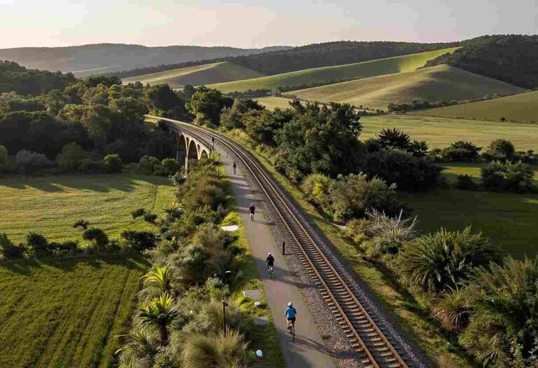 Railway line curves through green countryside with cyclists riding along a parallel path near a stone viaduct.