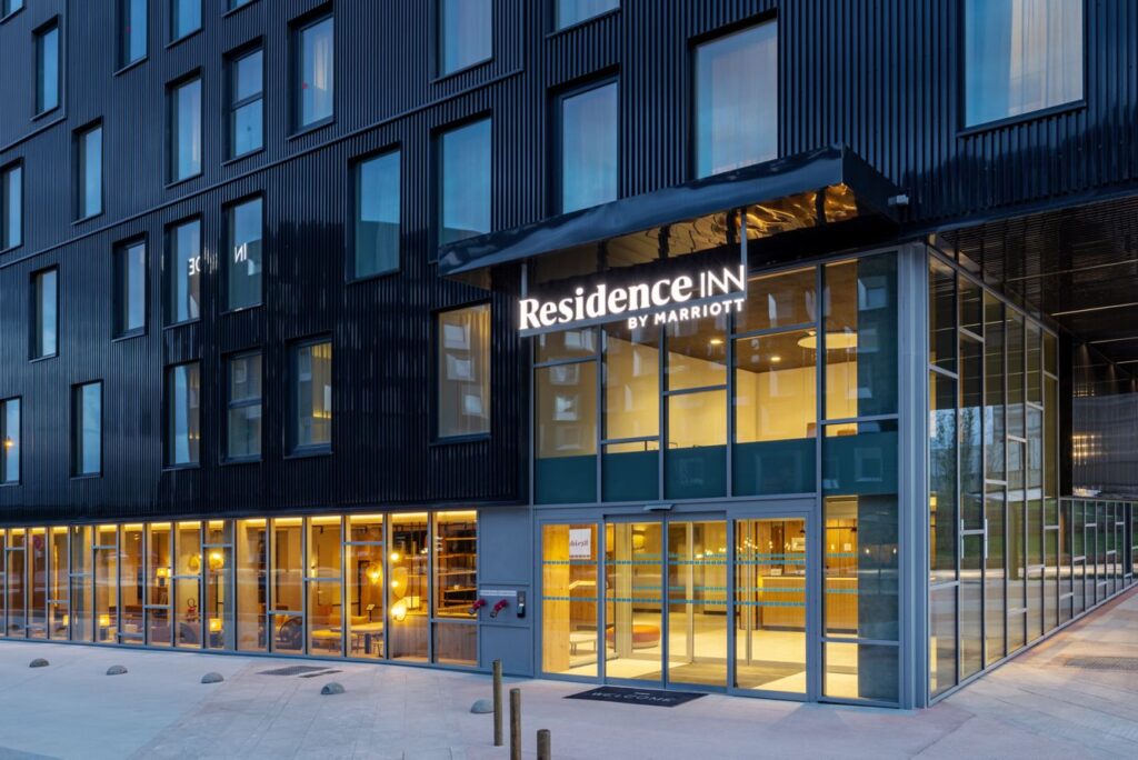 Residence Inn by Marriott entrance with glass doors and warm-lit lobby against a dark blue building façade at dusk.