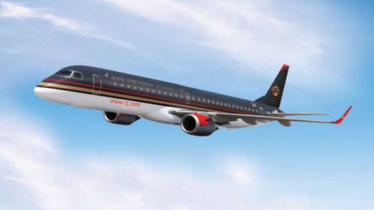Royal Jordanian passenger jet in dark livery flying through a blue sky with red winglets visible under bright clouds, side view profile