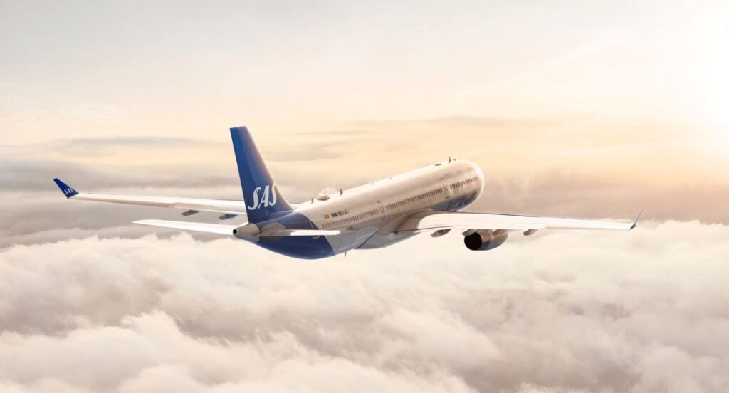 SAS commercial airplane flying high above fluffy clouds at sunset.
