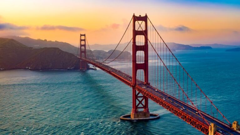 Golden Gate Bridge at sunset, towering red spans across the blue bay with hills in the distance.