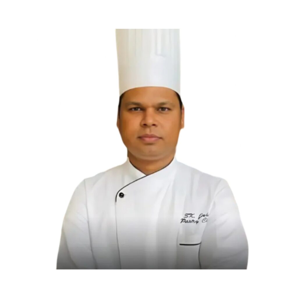 Professional chef in a white uniform and tall white hat, facing the camera with arms crossed.