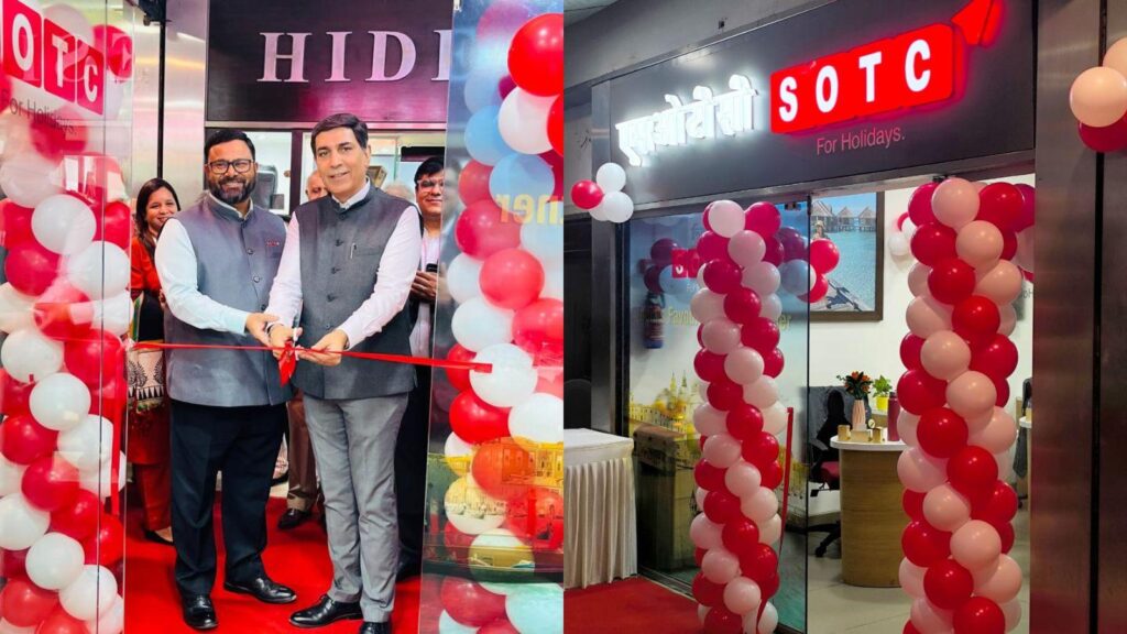 Two men cut a red ribbon at a store opening, flanked by balloons and onlookers in a showroom with 'SOTC' sign nearby.