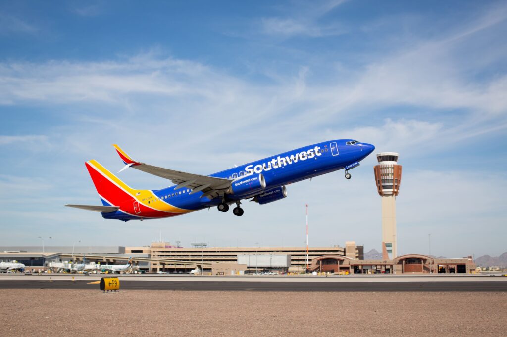 Southwest Airlines jet lifting off from runway with airport terminal and control tower in the background under a blue sky