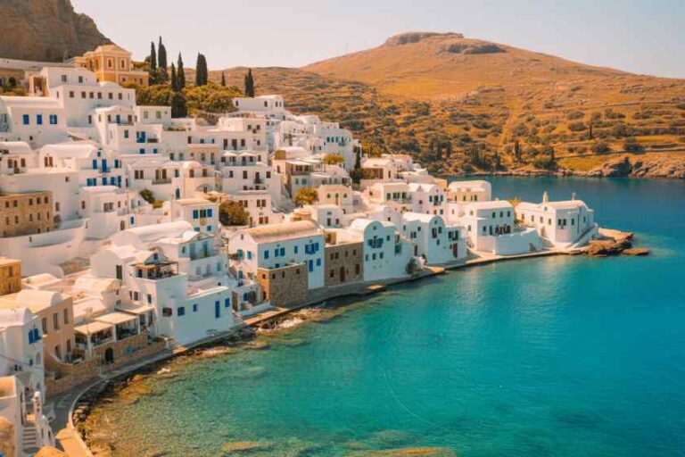 Whitewashed houses stack along a cliff, overlooking turquoise Aegean waters in a Greek coastal village (Santorini).