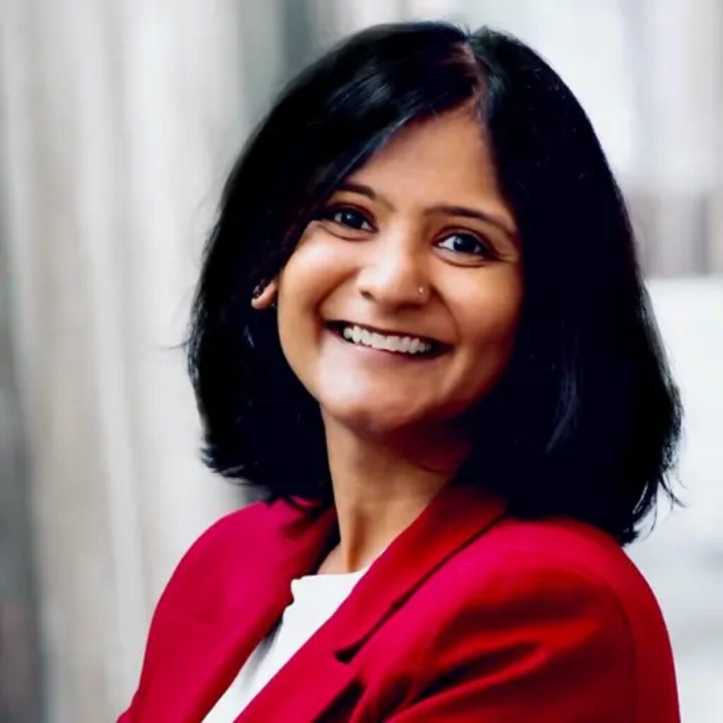 Smiling woman with shoulder-length black hair wearing a red blazer, facing slightly to the side.
