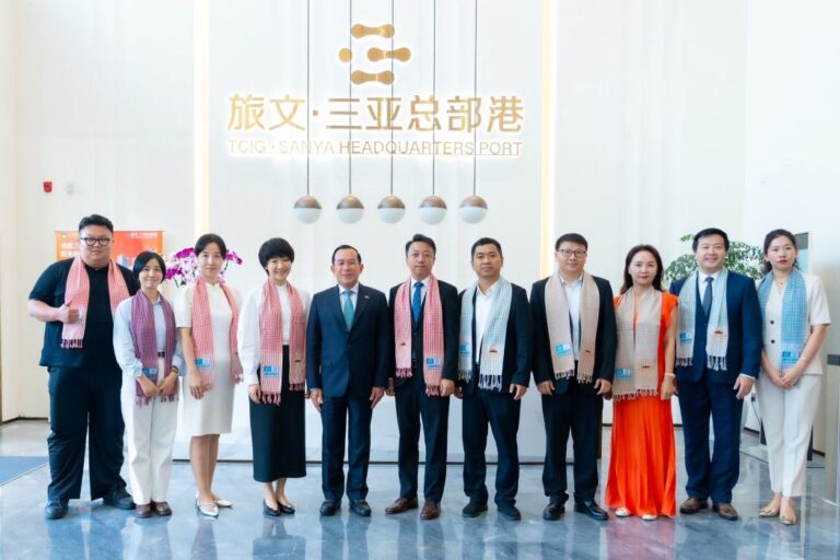 Twelve professionals in business attire pose for a group photo in a bright lobby with a TCIG Sanya Headquarters Port sign behind them.