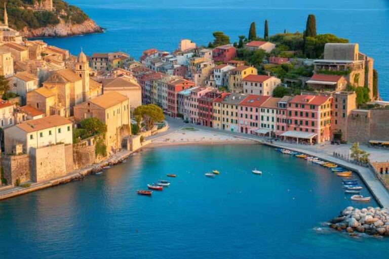 Colorful Mediterranean harbor town with pastel buildings lining a curved coastline and small boats in a blue bay.