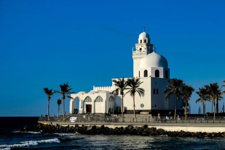White domed church on a sea wall, palm trees along the promenade under a clear blue sky.