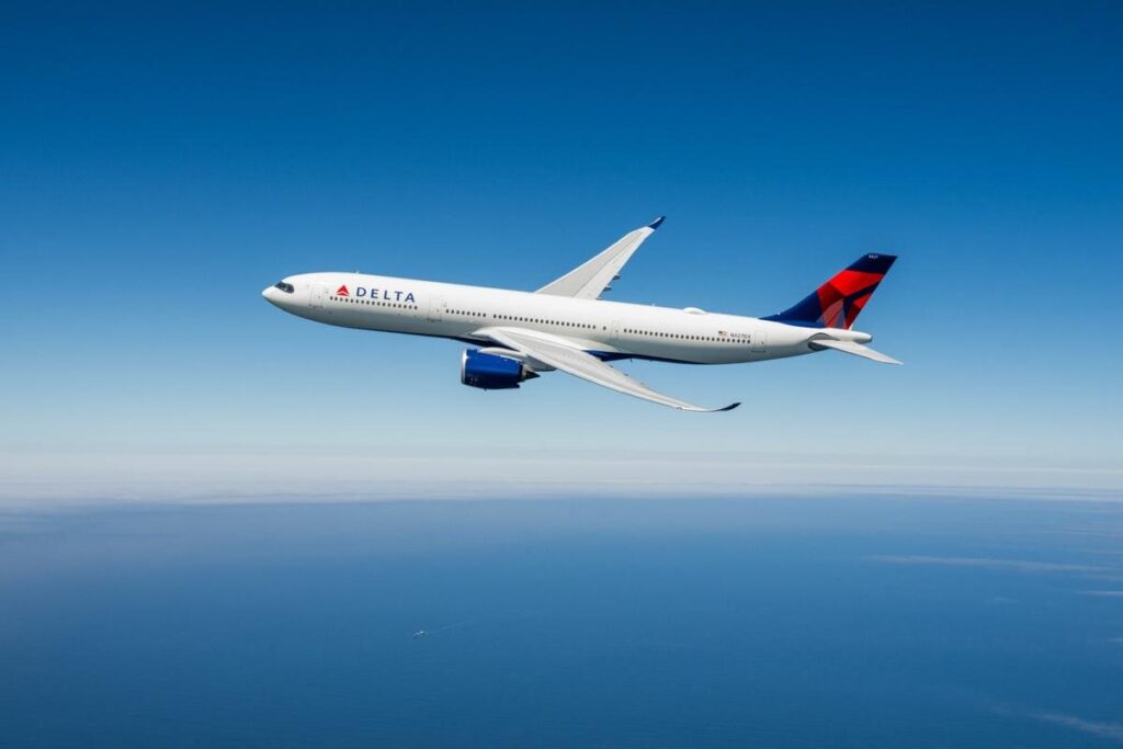 Delta Airlines airplane in cruising flight over the blue ocean under a clear sky with a red–blue tail