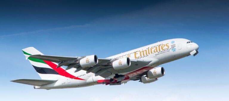 Emirates A380 jet in ascent against a blue sky, showing four engines and airline livery.