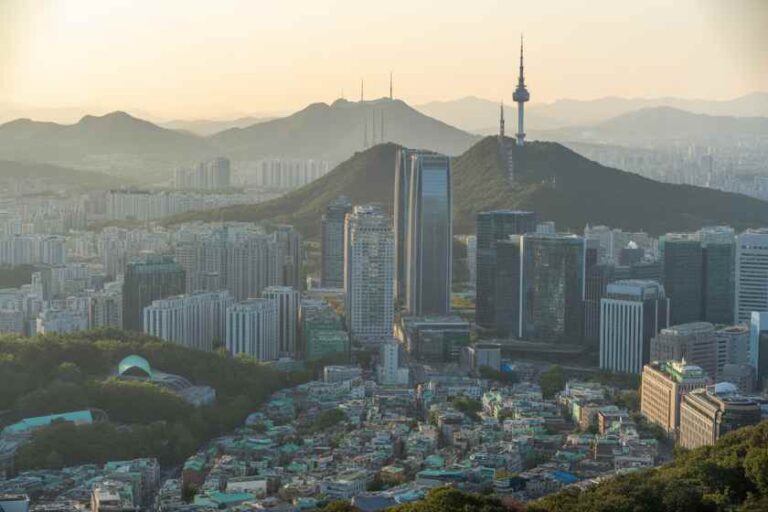 City skyline with high-rise buildings, hills in the background, and a tall communications tower on a hill.