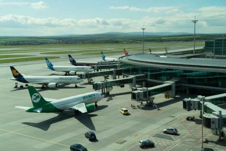 Aerial view of a busy airport gate with several airplanes parked at jet bridges and a clear runway in the distance.