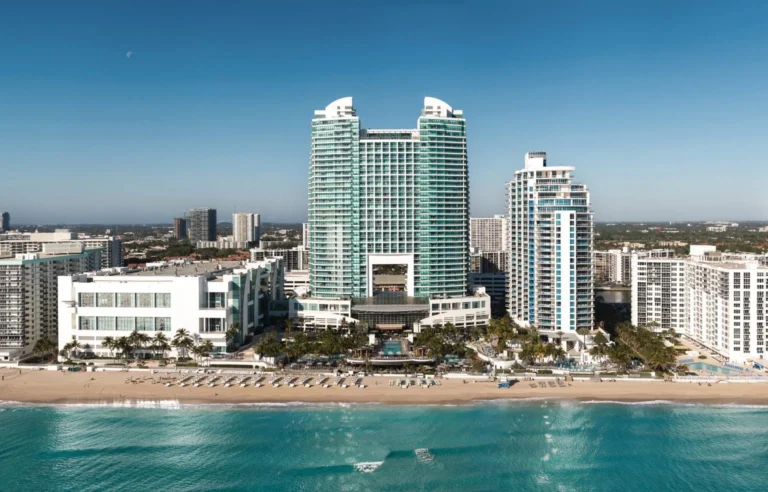 Aerial view of a beachfront city with a large glass hotel complex and white high-rises along a sandy shore.
