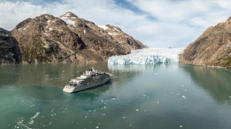 Passenger cruise ship sailing near a glacier calving into turquoise water between rocky mountains