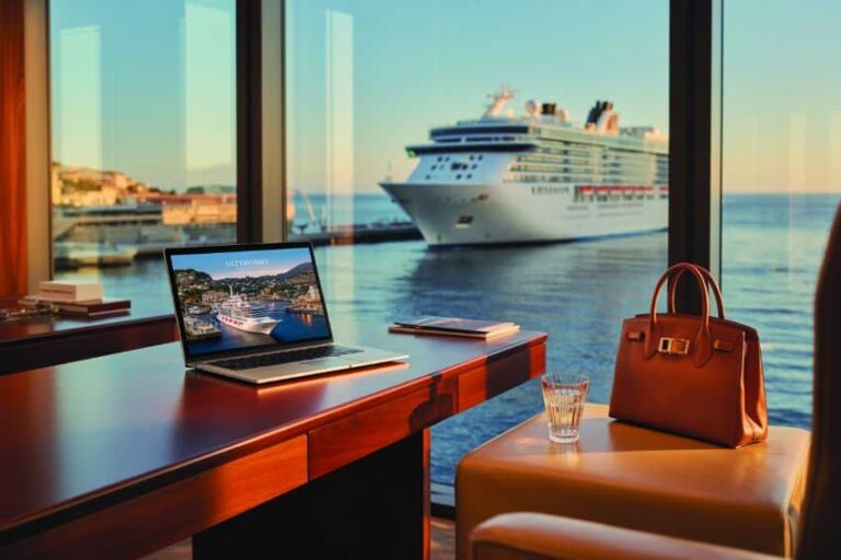 Luxurious cruise ship lounge seen from a sleek wooden desk with a laptop, handbag, and glass, overlooking a docked ship outside the window, sea view.