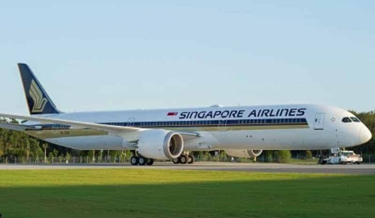 Singapore Airlines wide-body jet on a taxiway with engines visible and a clear blue sky behind.