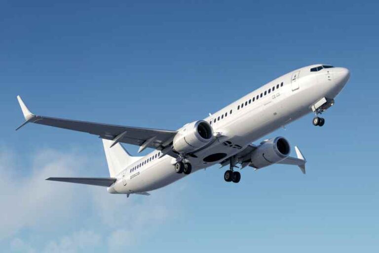 White passenger jet in ascent against a clear blue sky with landing gear down and flaps extended.