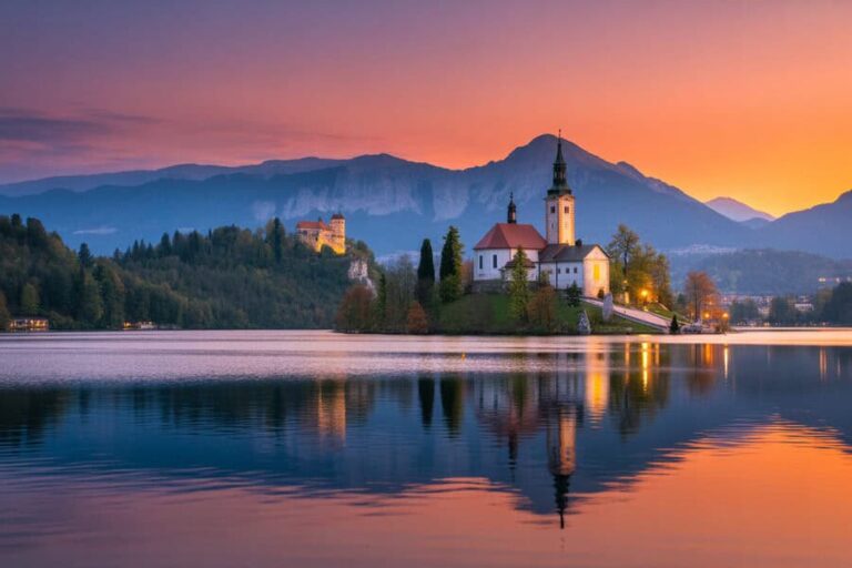 Sunset over Lake Bled with the church on the islet and a hilltop castle, reflected in the calm water.