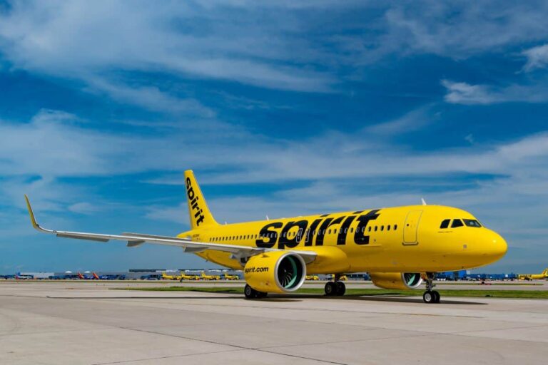 Bright yellow Spirit Airlines jet parked on runway with blue sky above he horizon behind it on a sunny day