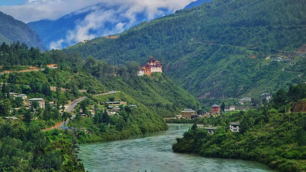 Lush river valley with a pagoda-style monastery perched on a hillside above a winding waterway.