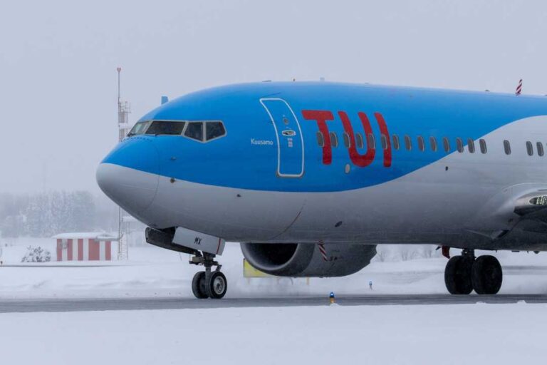 Front section of a blue TUI airplane parked on a snowy runway, showing cockpit windows, forward door, and landing gear.