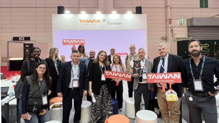 Group of professionals at a Taiwan trade show booth, posing with red 'Taiwan' signs and a panda cutout park image behind them