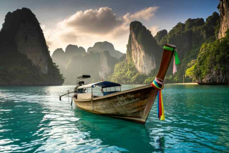 Long-tail Thai boat anchored in turquoise water with towering limestone cliffs at sunset