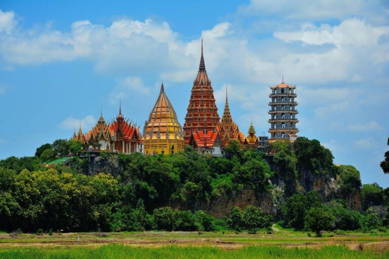Colorful Thai temple complex on a rocky hilltop with tall, ornate spires and a blue sky above.