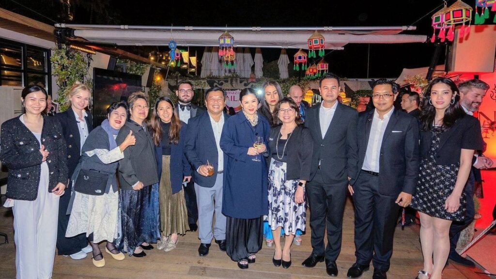 Group of adults in formal attire posing for a nighttime group photo at a festive outdoor event with colorful hanging lanterns above.
