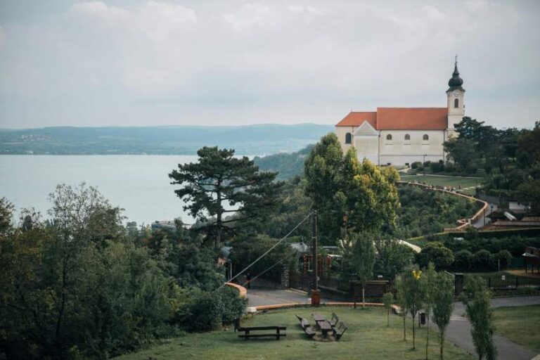 Hilltop white church with a red roof overlooking a lake, surrounded by trees and a park.