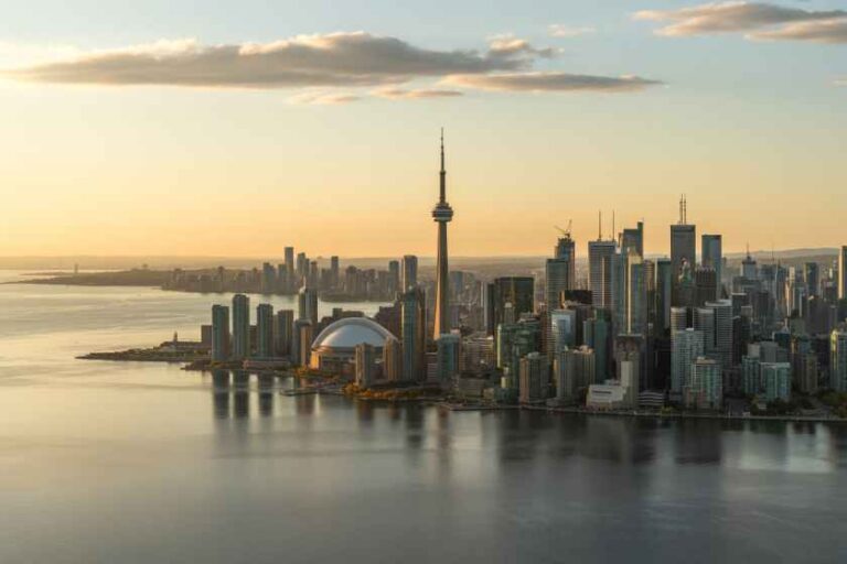 Sunset over Toronto skyline featuring the CN Tower and Rogers Centre along the harbour with calm water in the foreground.