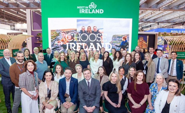 Group of diverse professionals posing for a photo at a Meet Ireland booth with a green backdrop reading 'Choose Ireland'.
