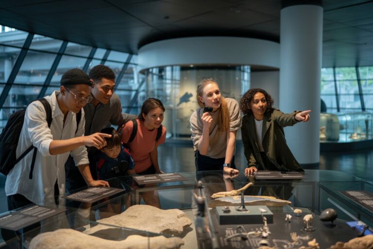 Group of five young people gathered around a museum display case, examining rocks and fossils.