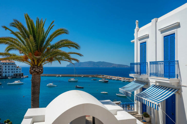 Bright blue sea in a Mediterranean harbor with white buildings, blue shutters, and striped awnings.