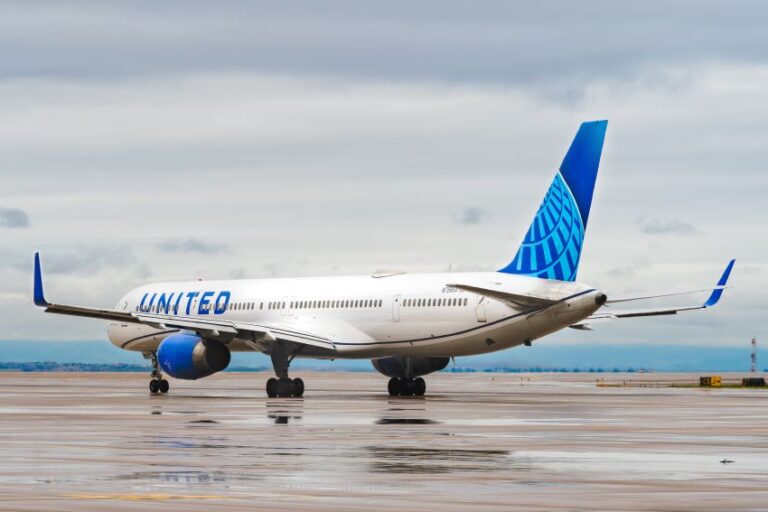 United Airlines plane parked on a wet runway with a blue globe-tail design on overcast day.