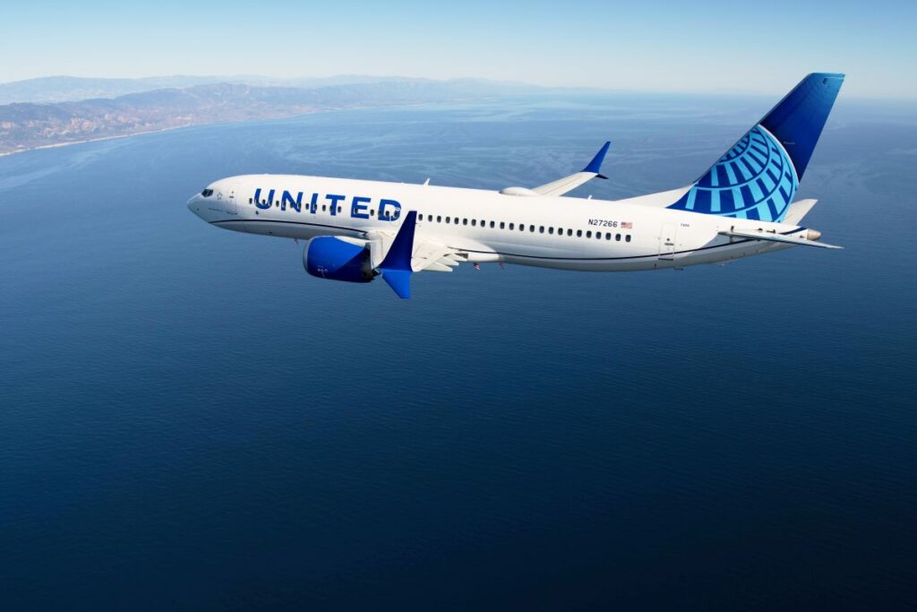 United Airlines jet flying over the ocean with coastline in the background, mid-flight.