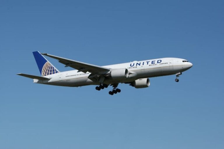 United Airlines wide‑body jet in approach with landing gear down against a clear blue sky, tail fin showing the U logo and globe emblem