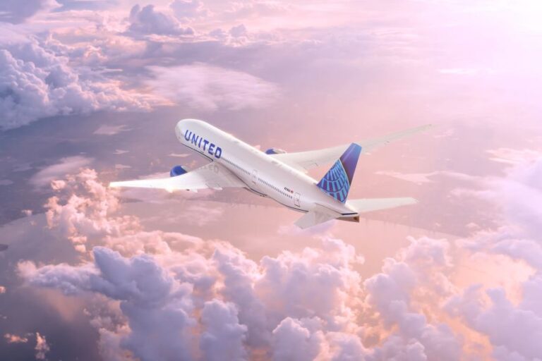 United Airlines jet cruising above pink-tinged clouds in a sunset sky? mid-flight view of a white and blue plane with the United logo on the fuselage and tail.