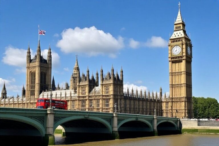 Houses of Parliament and Big Ben beside Westminster Bridge with a red double-decker bus crossing the bridge on a sunny day.