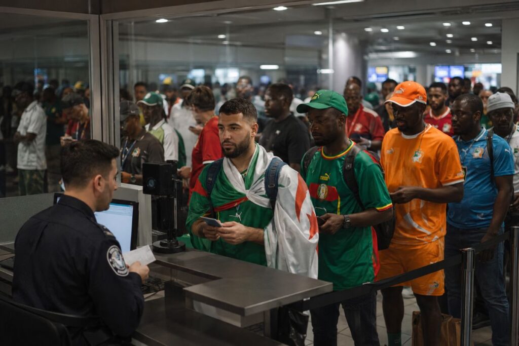 Group of men in colorful jerseys waiting in line at an airport security checkpoint while a security officer checks documents at a desk.
