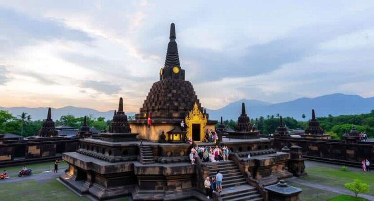 Ancient stone Buddhist temple with a central stupa and tiered platforms, visitors climbing the steps at dusk.