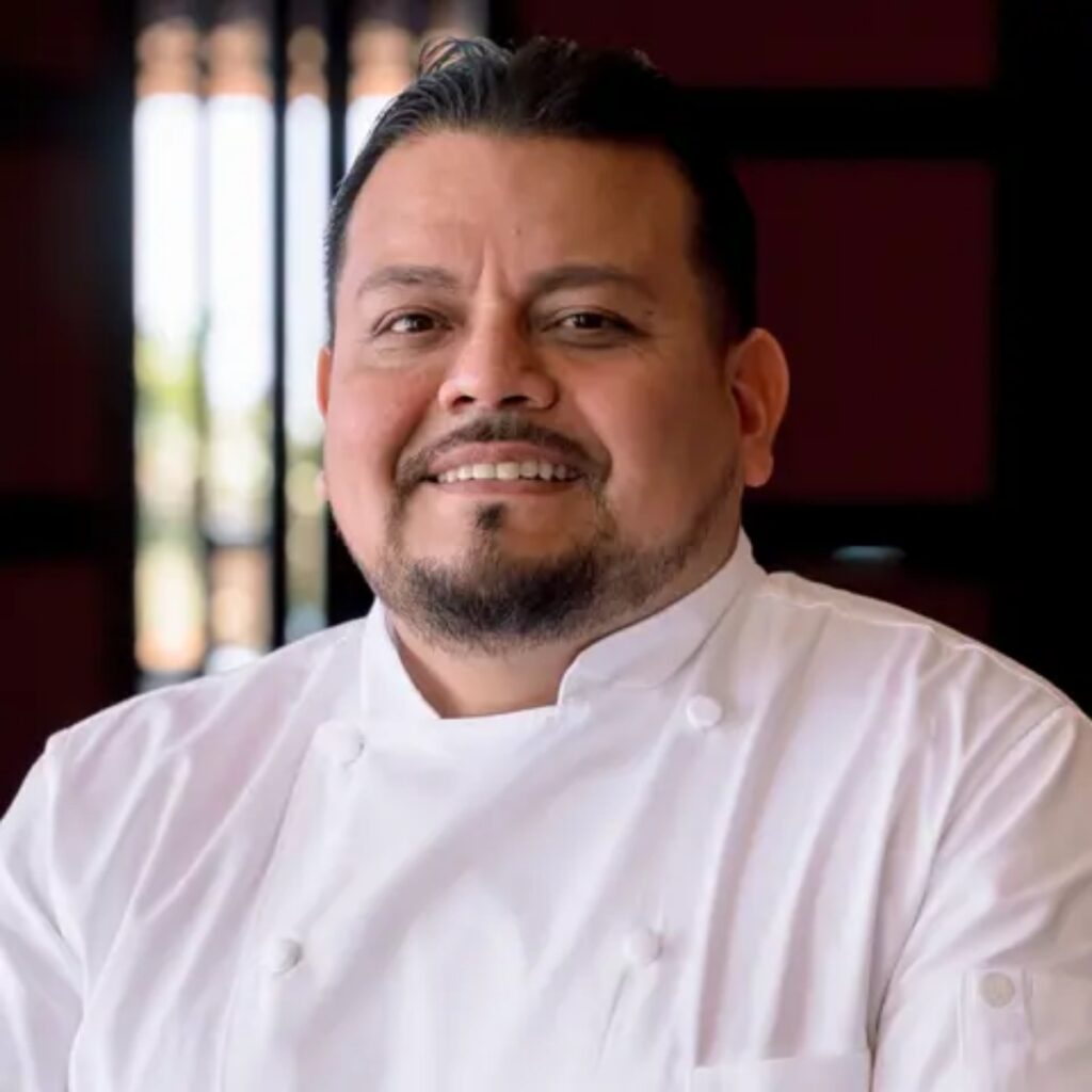 Smiling chef in a white chef coat in a restaurant setting.