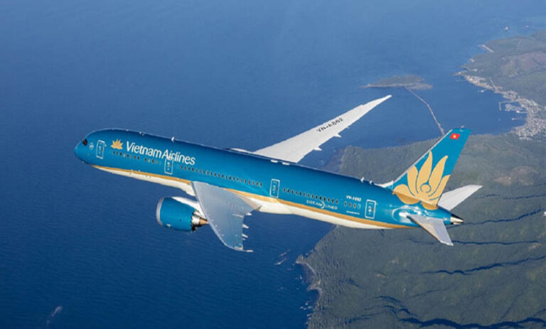 Vietnam Airlines passenger jet in blue livery flying above a coastline and sea cliffs