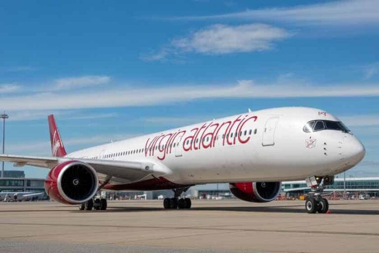 Virgin Atlantic wide-body aircraft on the tarmac under a blue sky, front view showing the branding on the fuselage and red engine and tail fin.
