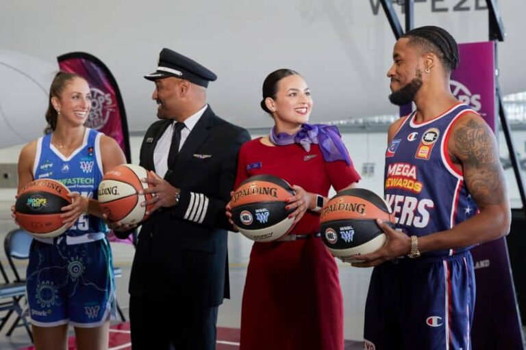 Four people pose with basketballs at a sports event: two players in blue uniforms, a pilot, and a woman in a red dress, all smiling.