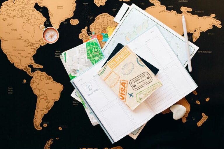 Overhead view of travel planning items on a world map: passport, maps, notebook, compass, and pen.