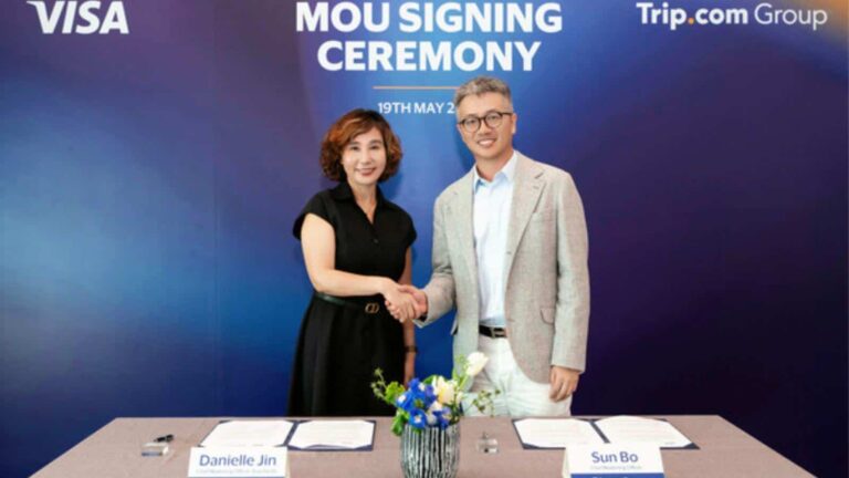 Danielle Jin and Sun Bo shake hands at an MOU signing ceremony, with documents on a table and a blue backdrop.
