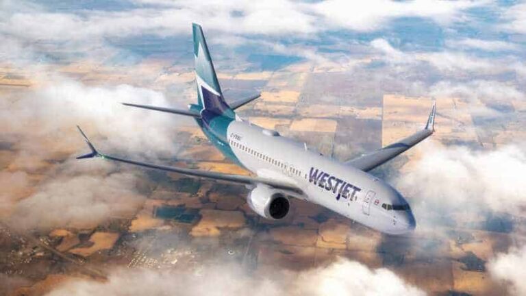 WestJet airplane flying above a patchwork of fields, partially above clouds.